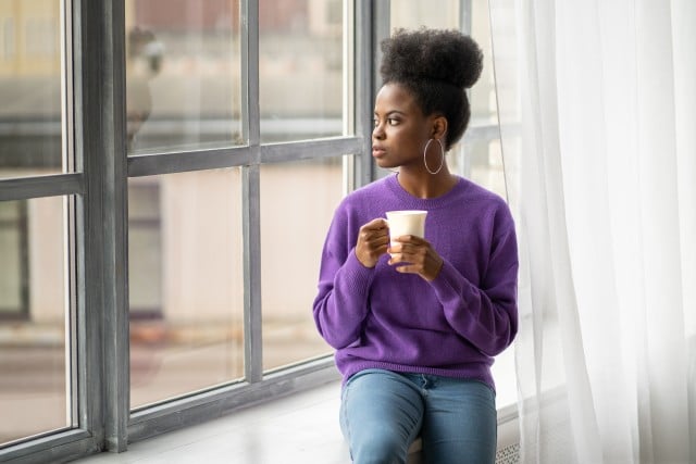 Frau, die nachdenklich am Fenster sitzt und sich fragt: 'Liebe ich ihn noch?'